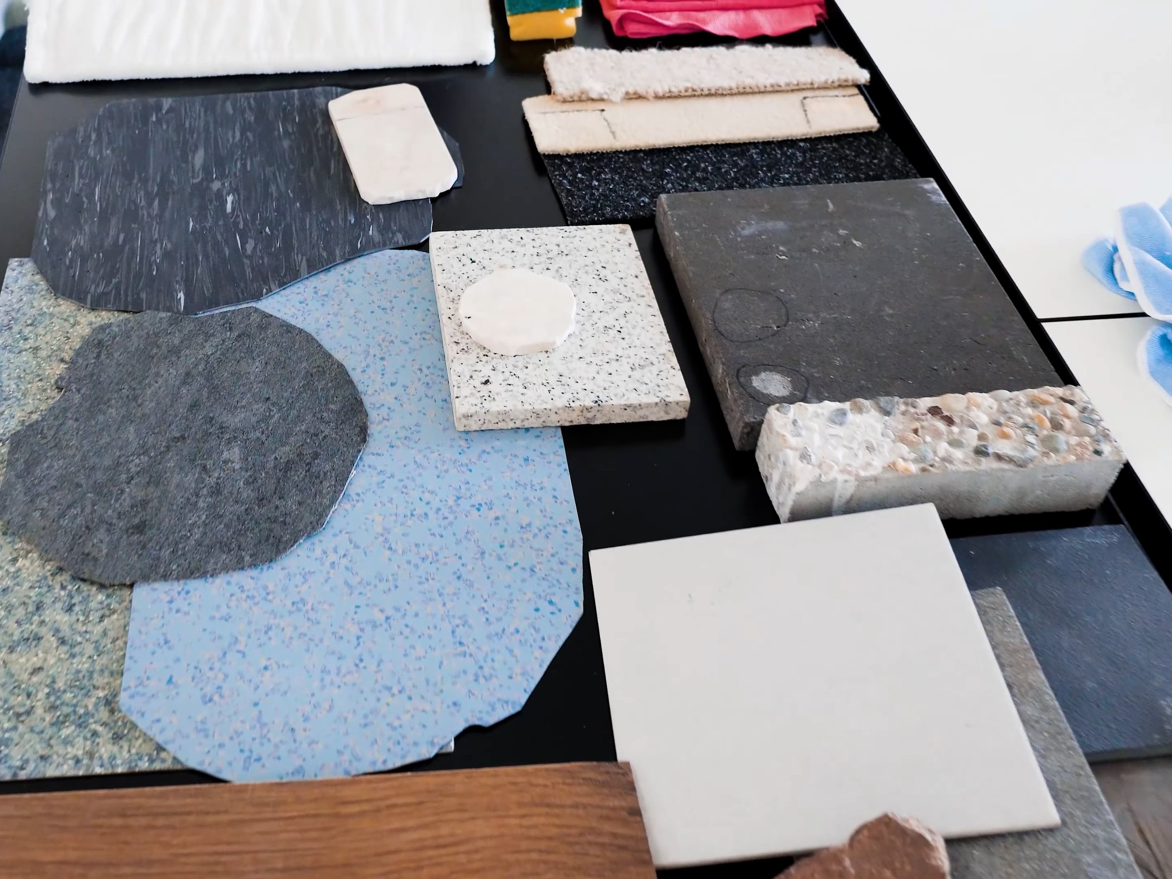 Muster verschiedener Bodenbeläge auf einem Tisch: Naturstein, Terrazzo, Linoleum, Fliese, Holzoptik und Teppich