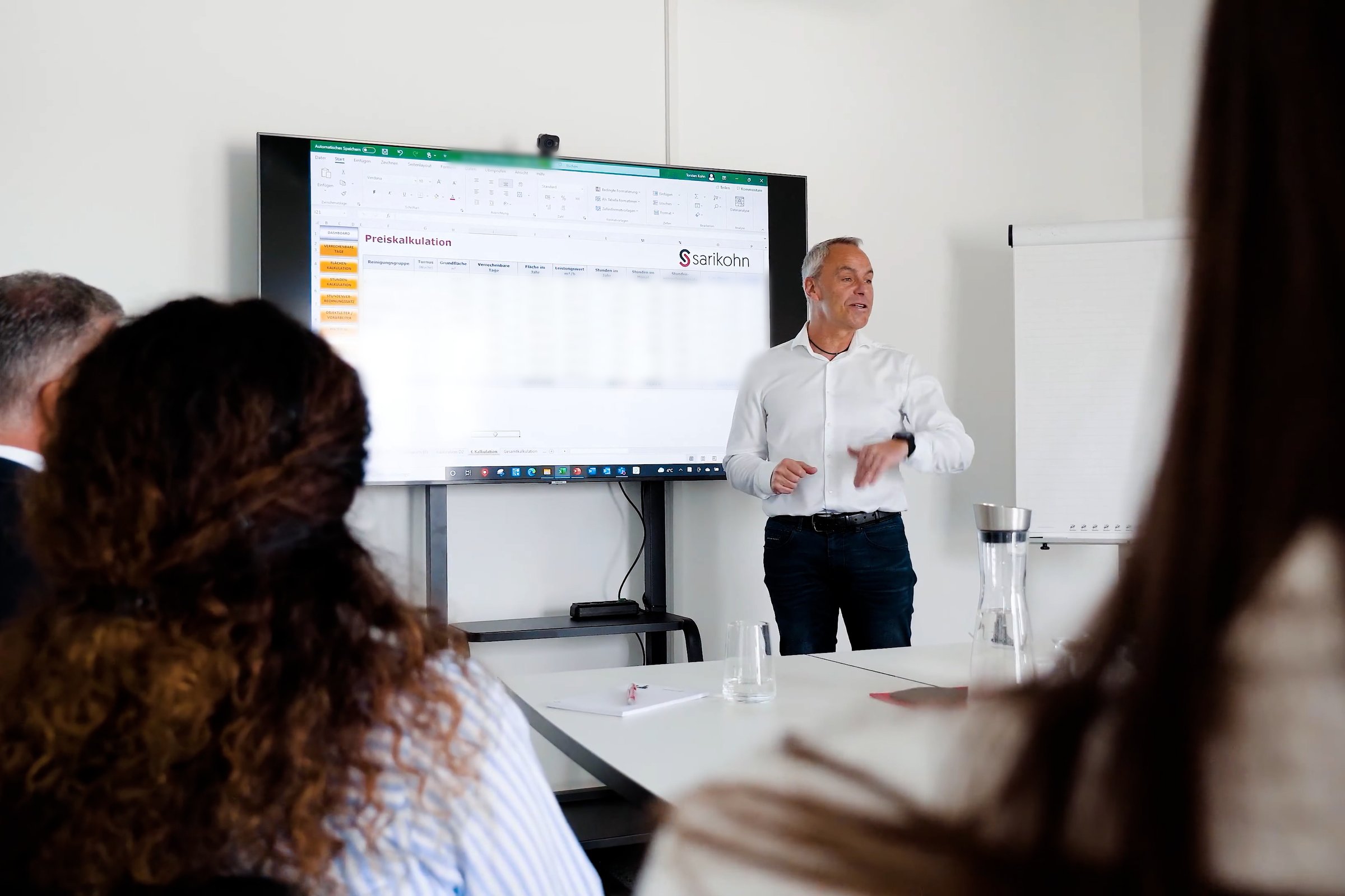 Seminar: Erläuterung einer Preiskalkulation am Großbildschirm, Teilnehmende von hinten